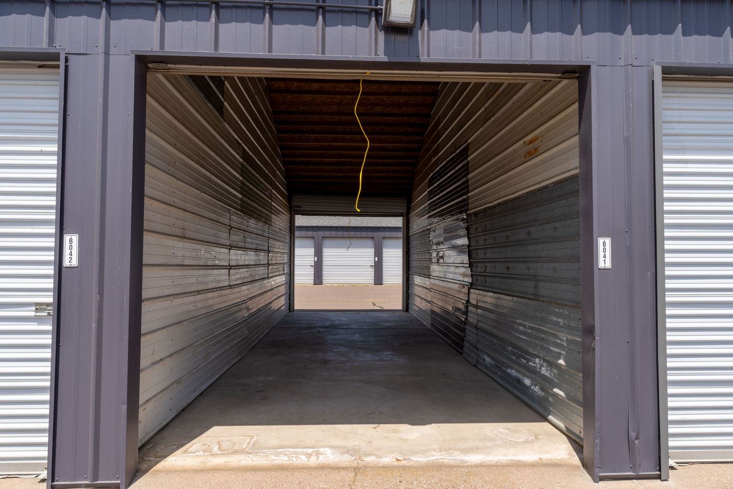 Long corridor view of multiple storage units with roll-up metal doors in a self-storage facility.