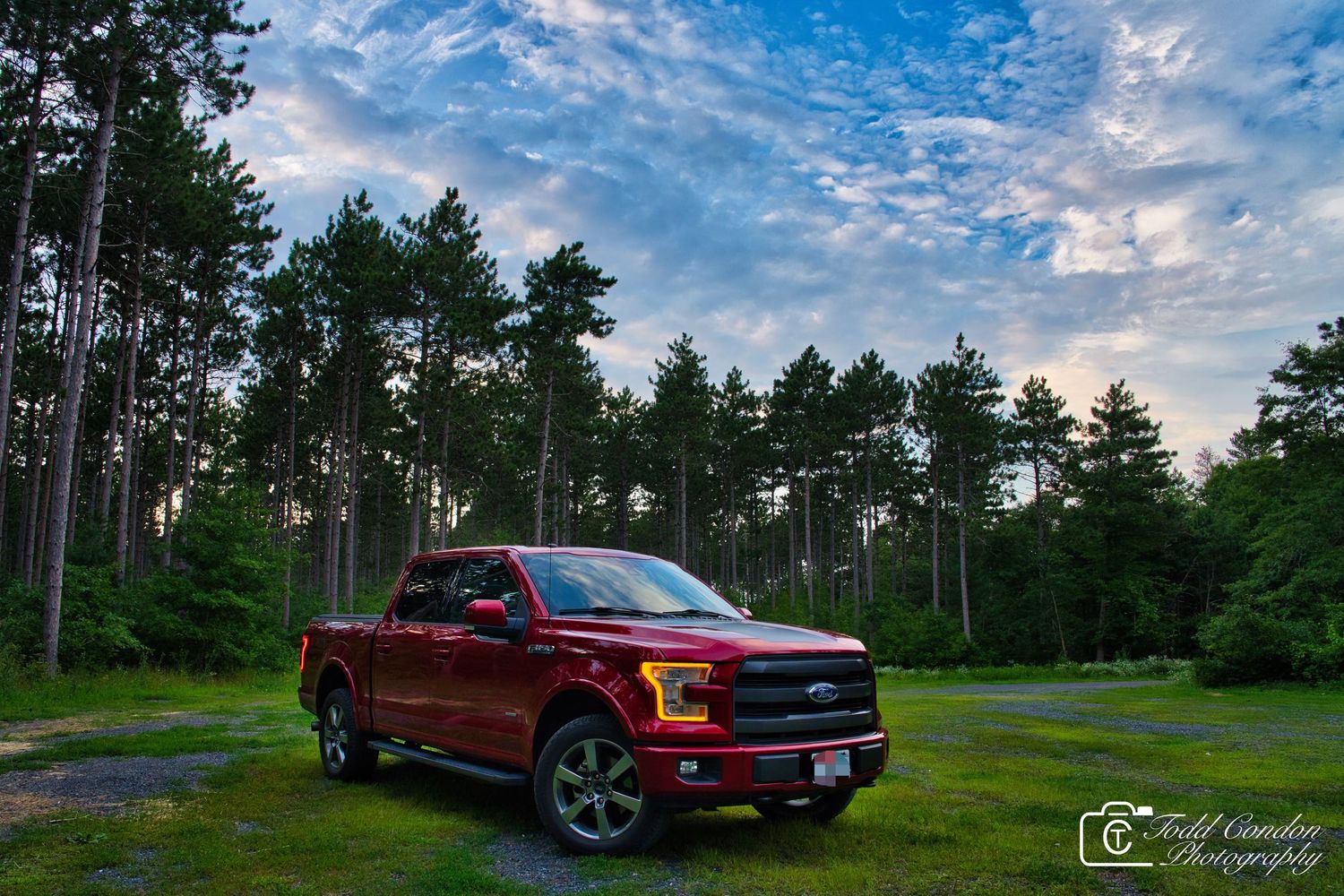 Panoramic view of a red pickup truck parked in a forest clearing during sunset.