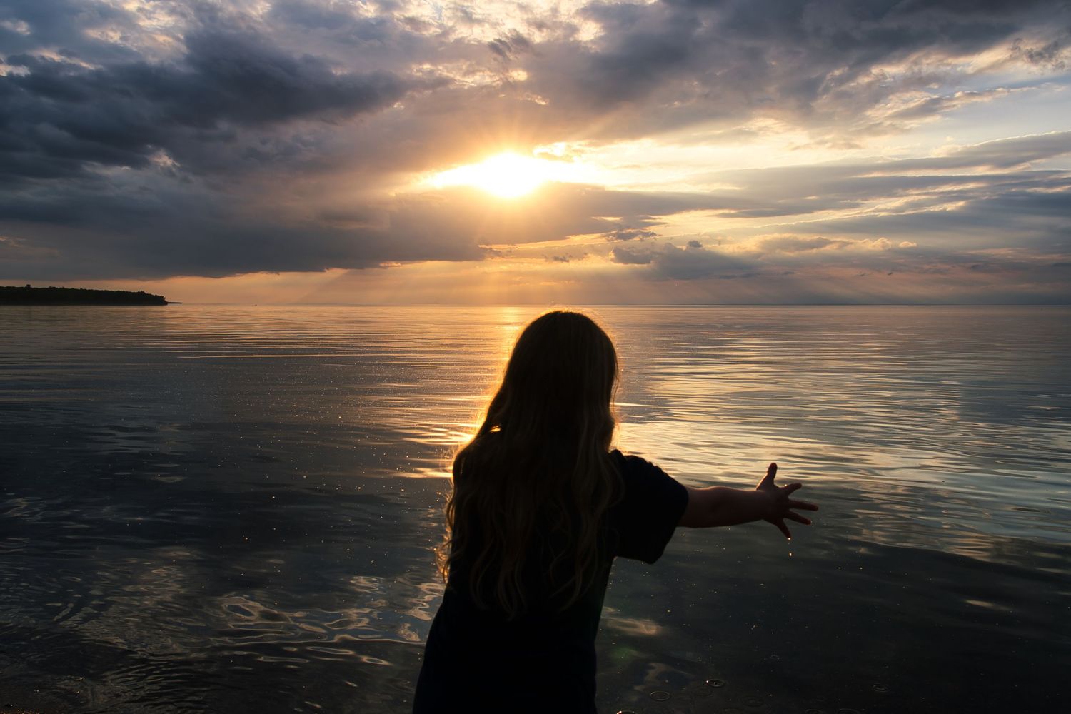 Dramatic sunset over calm ocean waters with silhouettes against the horizon.