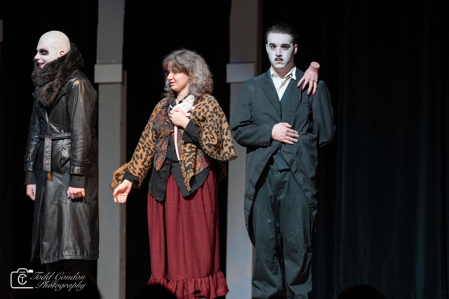 Actors in Victorian-era costumes perform on a dimly lit stage during a theatrical production.