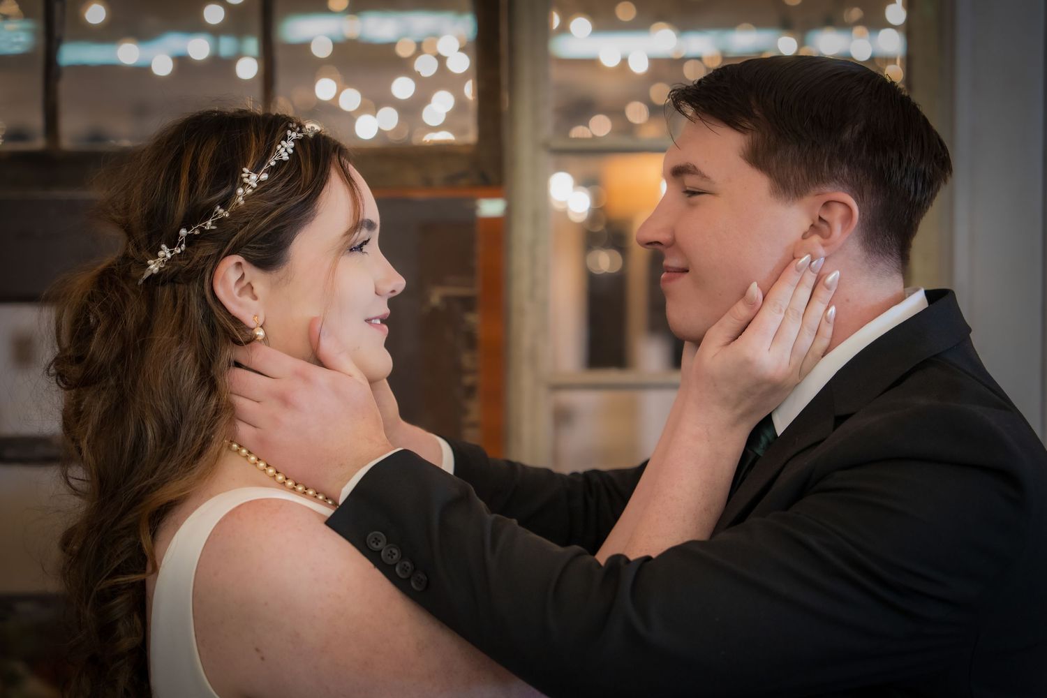 A couple shares a romantic kiss during their wedding celebration with bokeh lights in the background.