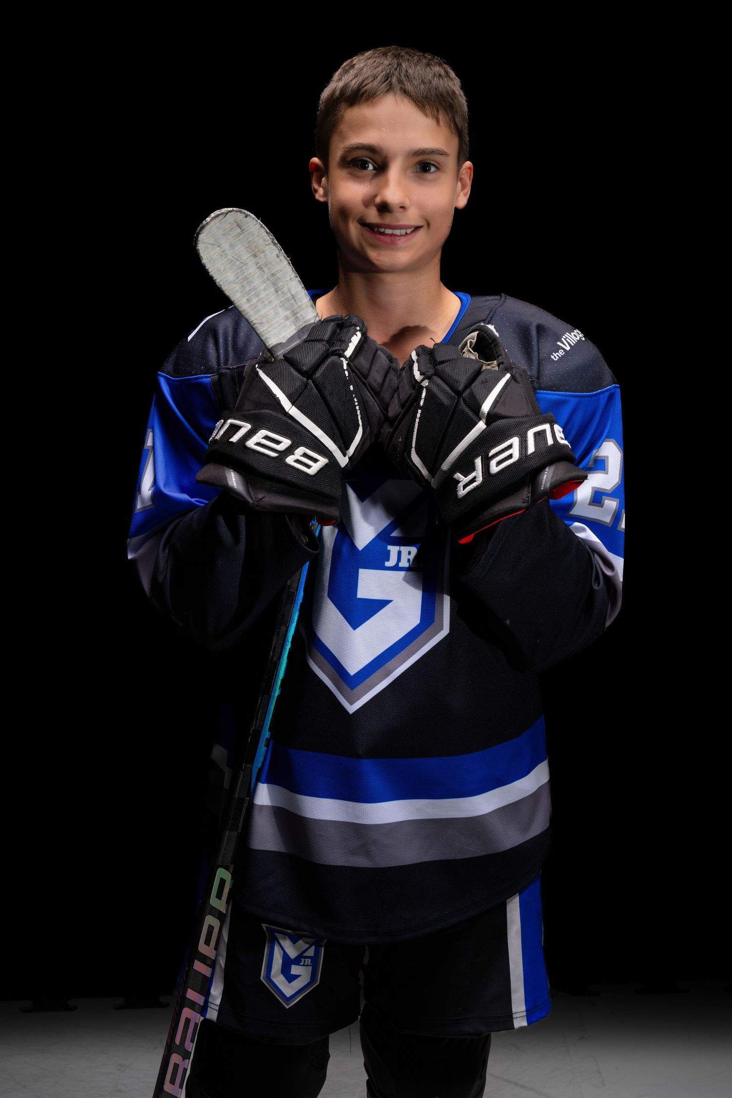 Hockey player poses in black and blue team jersey with matching gloves against dark background.