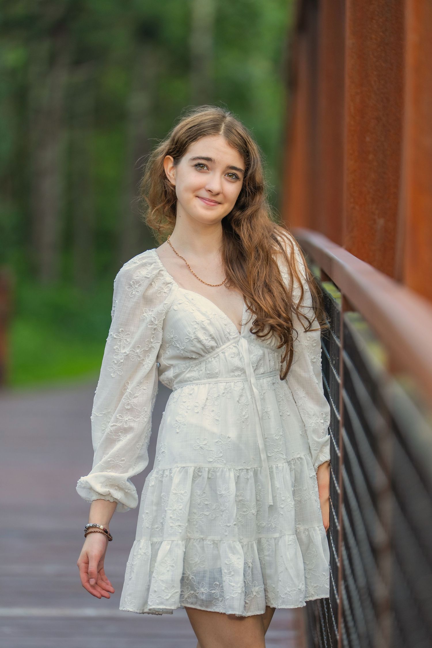 A young person in a white lace dress with puff sleeves poses outdoors against a natural green background.