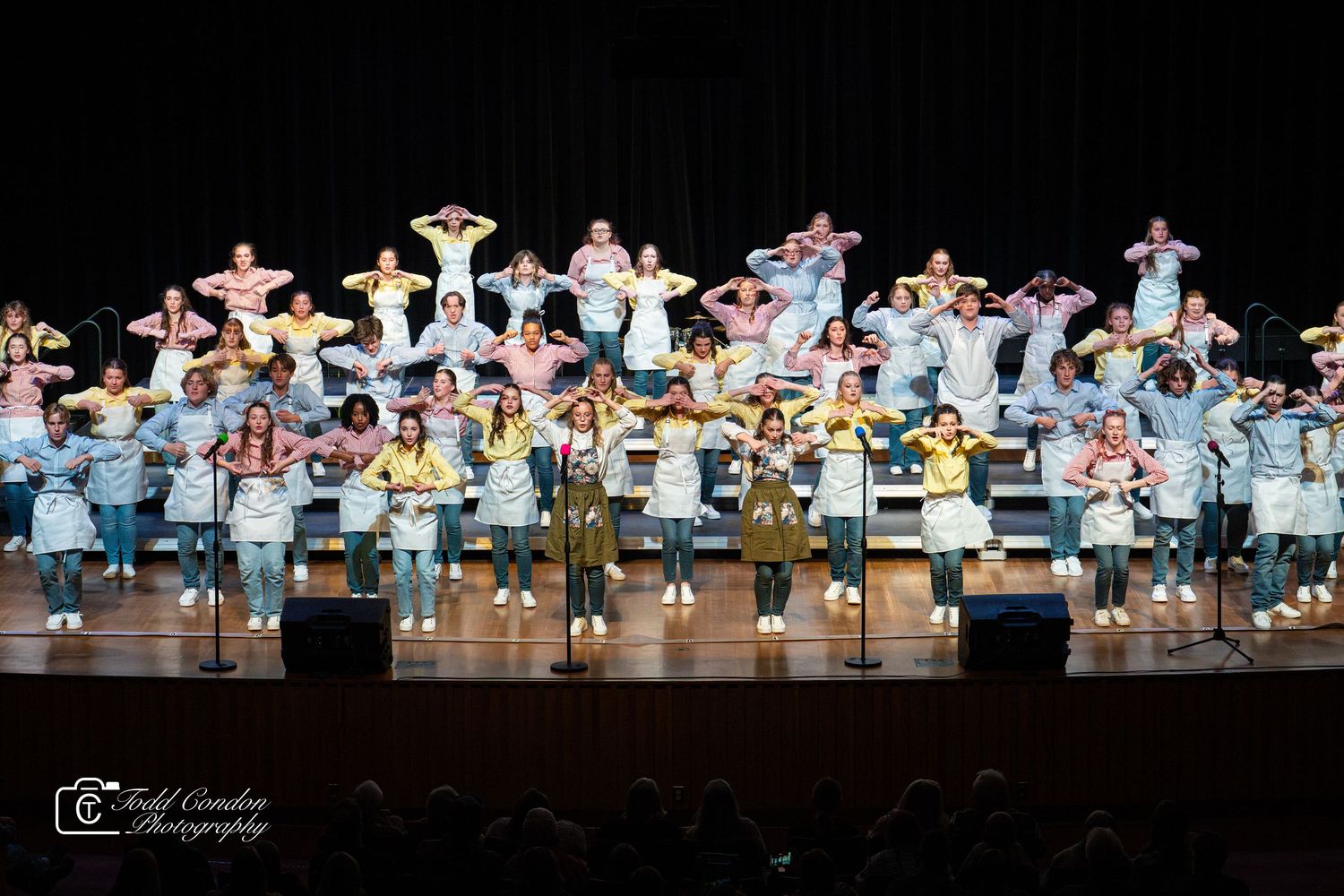 Dance performers in white costumes line up across a dark stage during a synchronized performance.