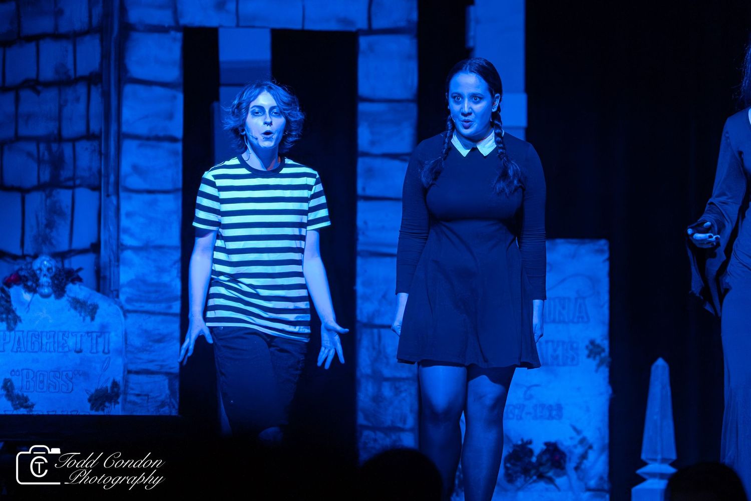 A stage performance scene lit in blue featuring actors in black and white striped costumes during a theatrical production.
