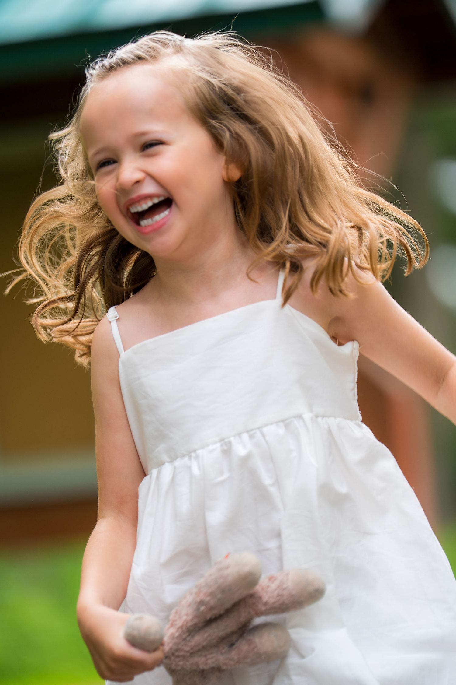 A child in a white dress spins and twirls joyfully outdoors with blonde hair flowing in the breeze.