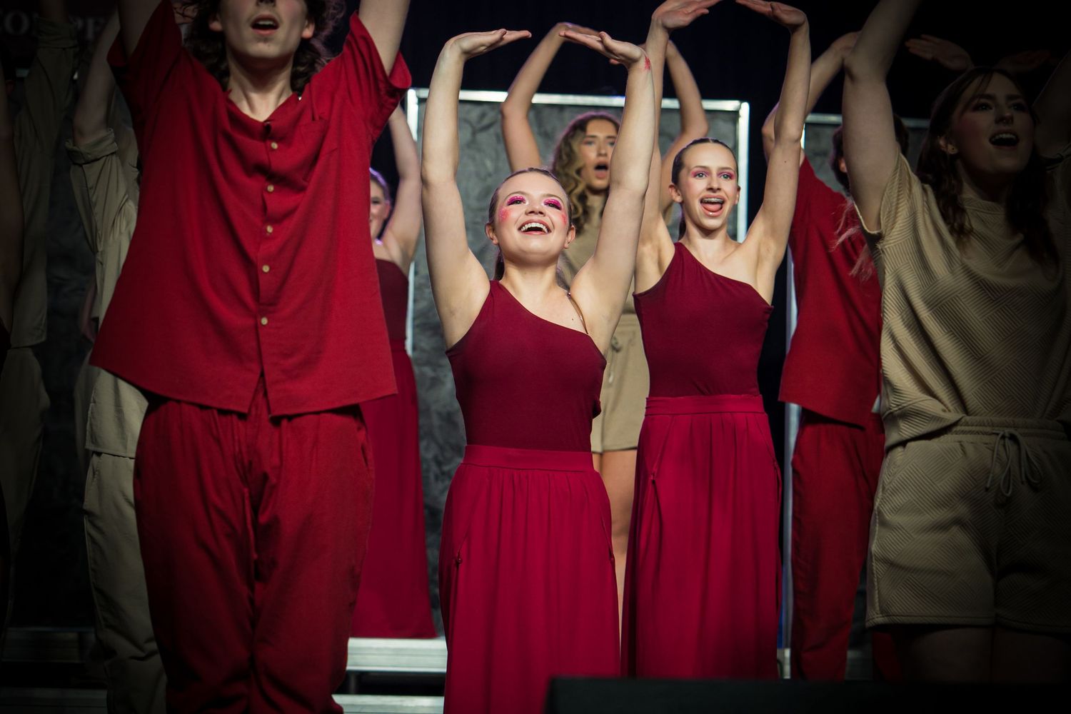 Performers in flowing red dresses raise their arms during an energetic stage performance.