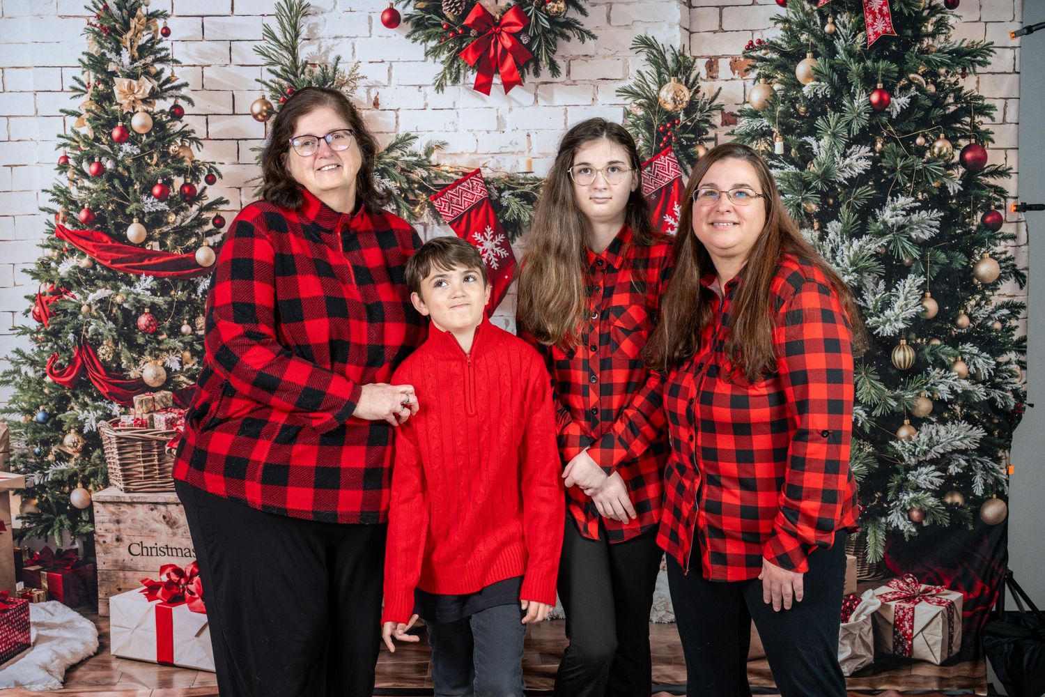 A group wearing matching red and black buffalo plaid flannel shirts poses in front of decorated Christmas trees and wreaths.