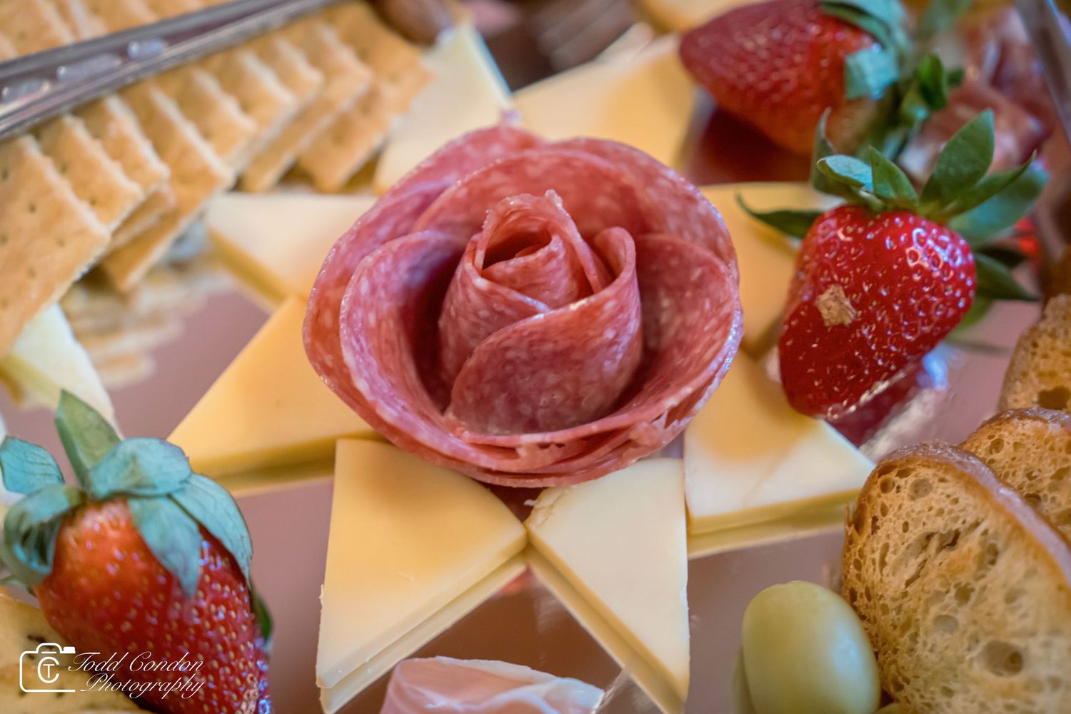Elegant charcuterie board featuring a salami rose centerpiece, sliced cheeses, fresh strawberries, crackers, and olives.