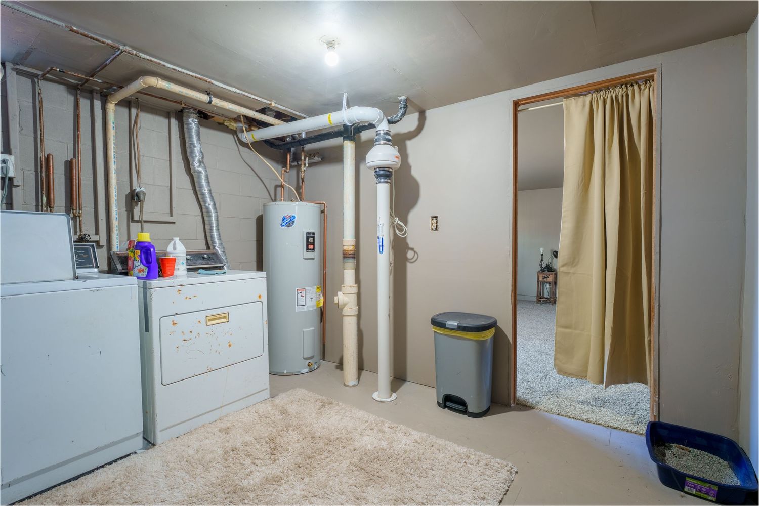 Panoramic view of a basement utility room with water heater, furnace, and gold curtains dividing the space.