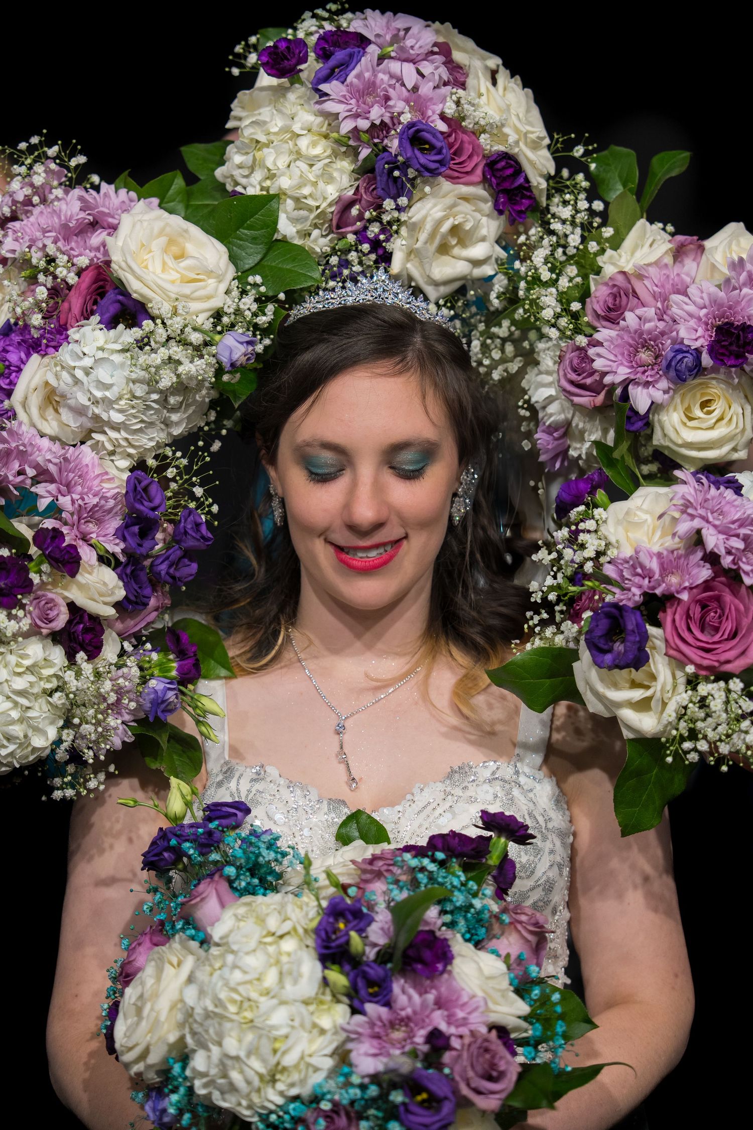 A bridal portrait with purple and white roses, baby's breath, and turquoise floral accents against a dark background.