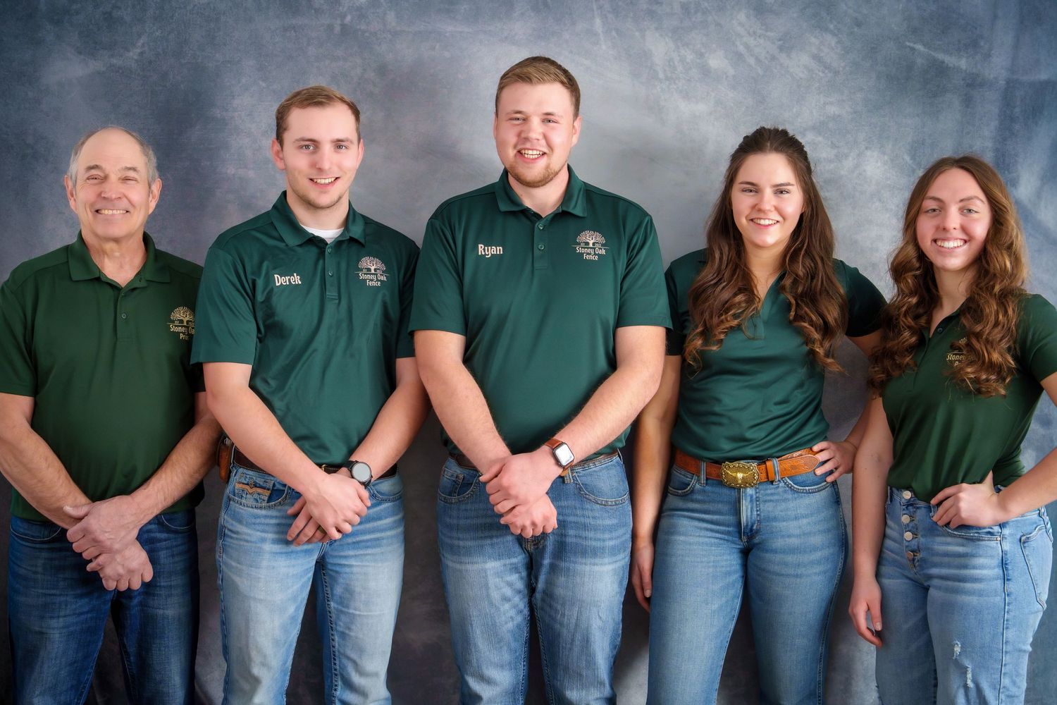 Five people in matching green polo shirts and jeans pose together for a professional group photo.