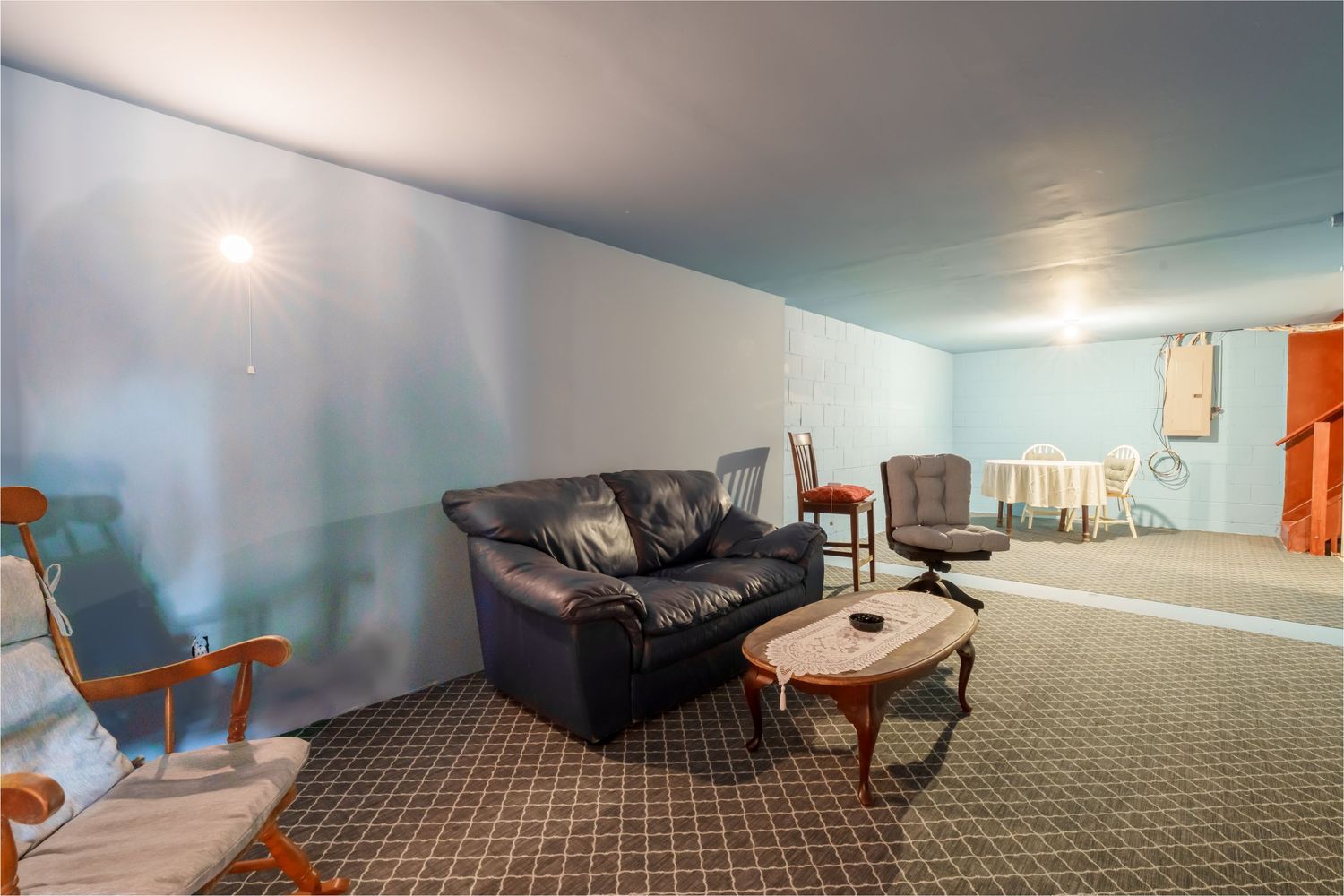 A panoramic view of a finished basement room with light blue walls, carpet flooring, and recessed lighting.