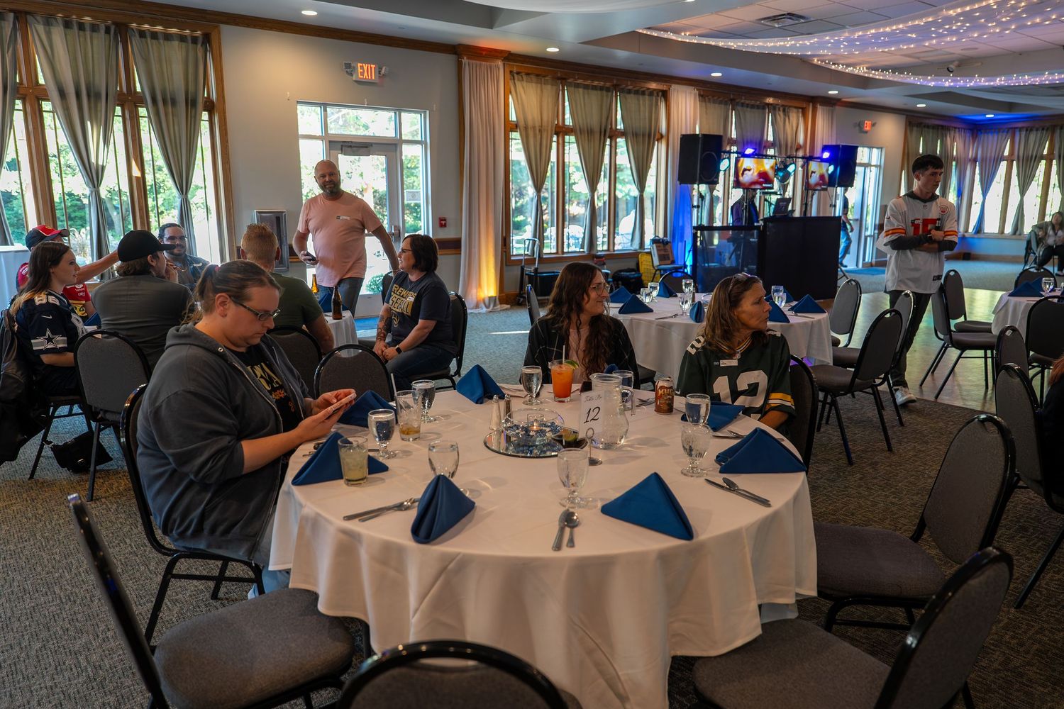 A banquet room setup with round tables and chairs in a bright space with large windows overlooking water views.