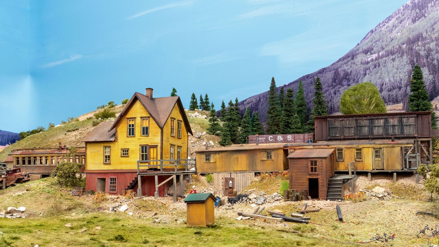 Abandoned mining town buildings with yellow and brown structures nestled against mountain backdrop in Colorado.