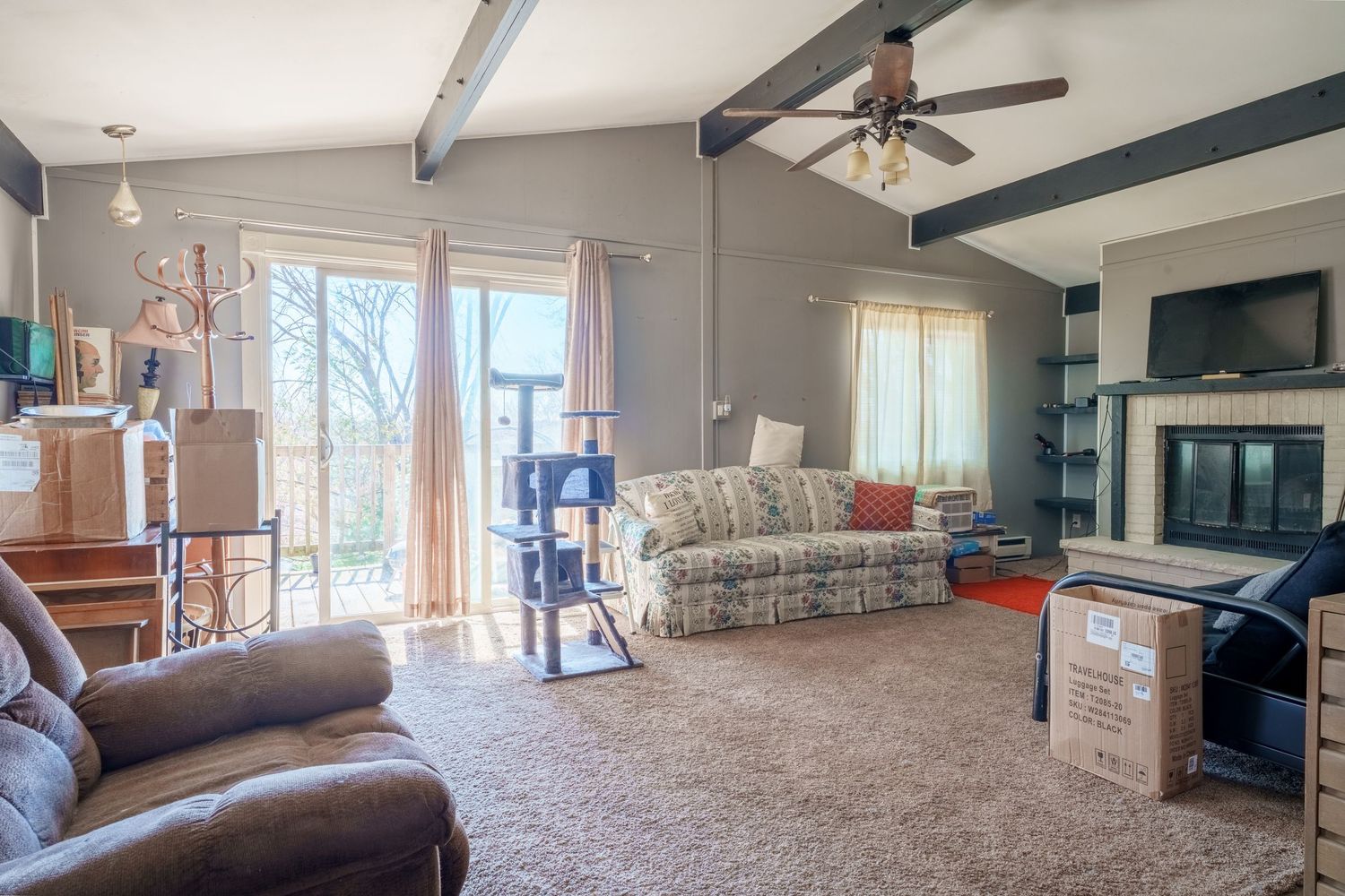 Panoramic view of a spacious living room with beige carpet, ceiling fan, and large windows letting in natural light.