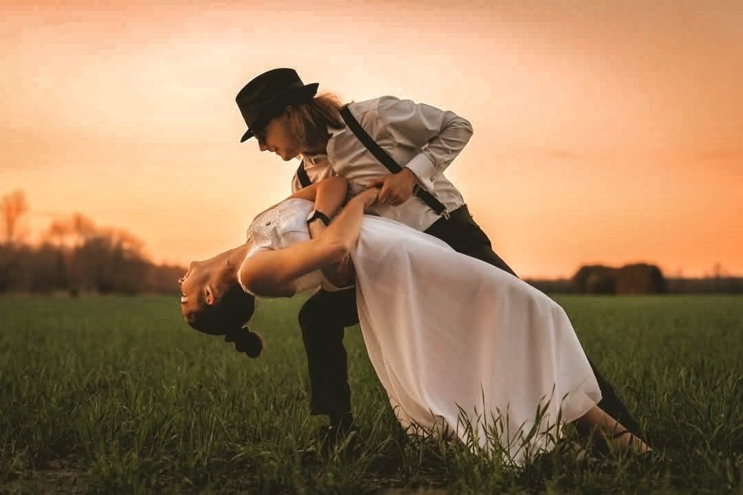 Couple in formal wedding attire embraces in a golden sunset field creating a romantic silhouette.