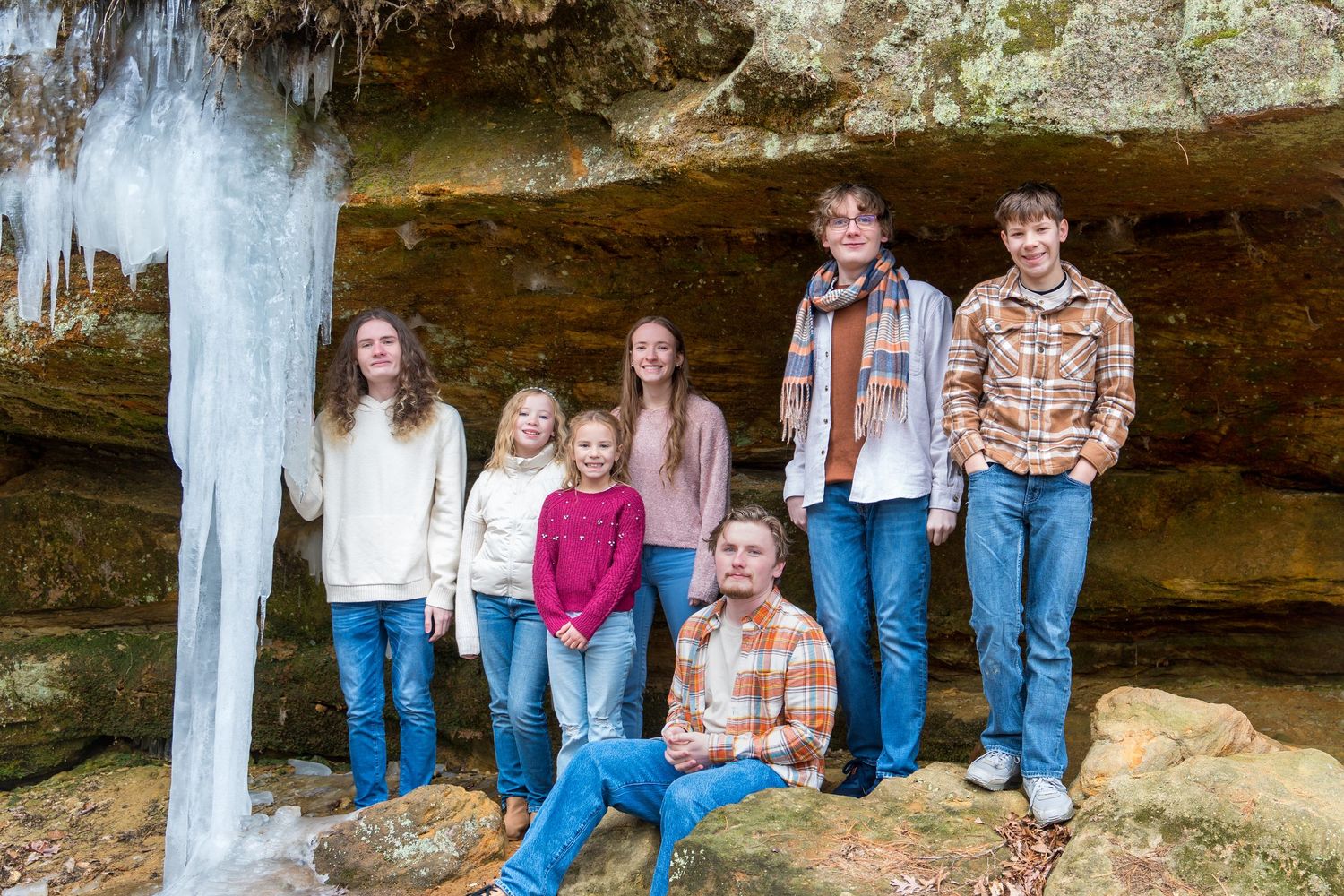 Group gathered under a large rock overhang in natural setting.