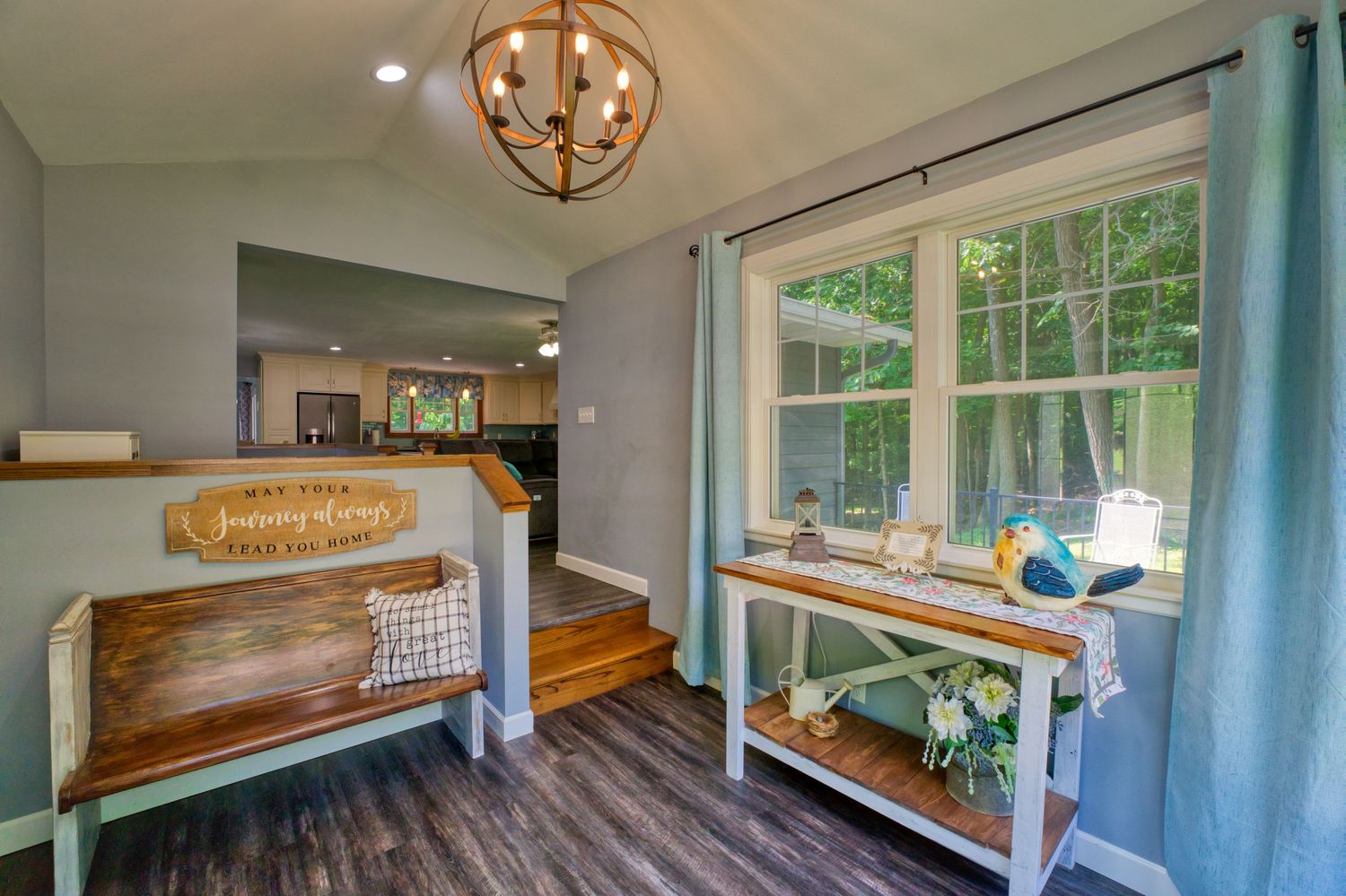 Bright entryway with rustic wooden bench, console table, teal curtains, chandelier, and hardwood floors.