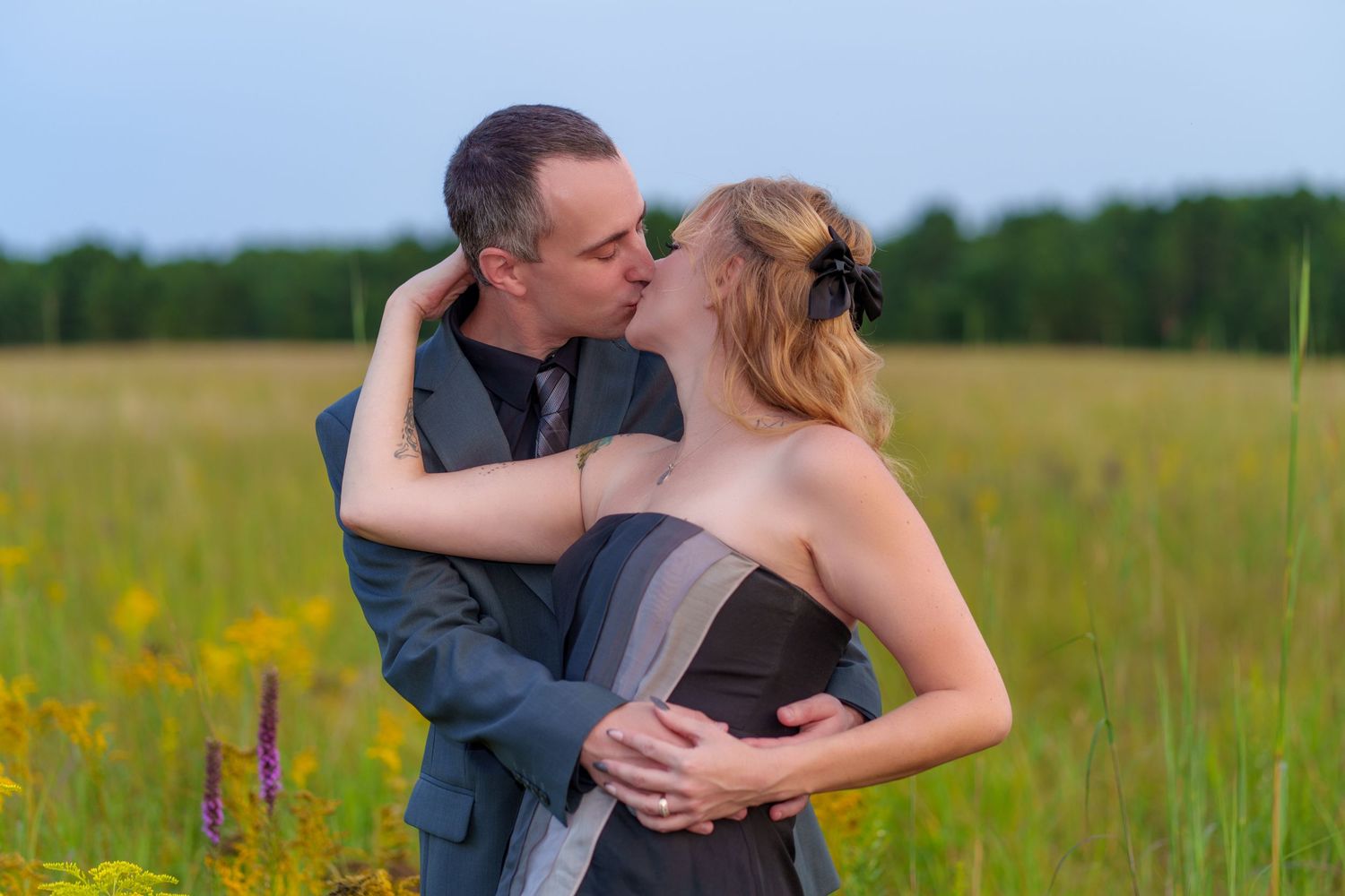 Couple sharing a romantic kiss in a wildflower meadow, man in gray suit embracing woman in elegant gray dress.