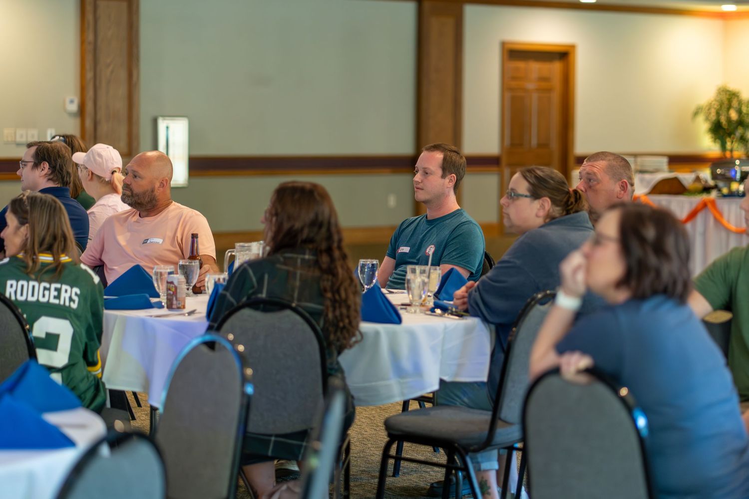 People gathered at round tables in a conference or meeting room setting during a social event.