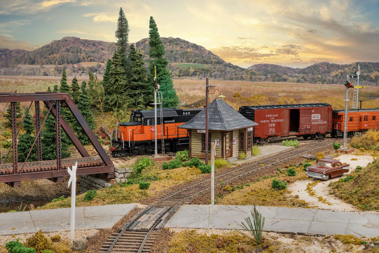 Scenic model train layout featuring vintage railcars winding through mountainous terrain at sunset.