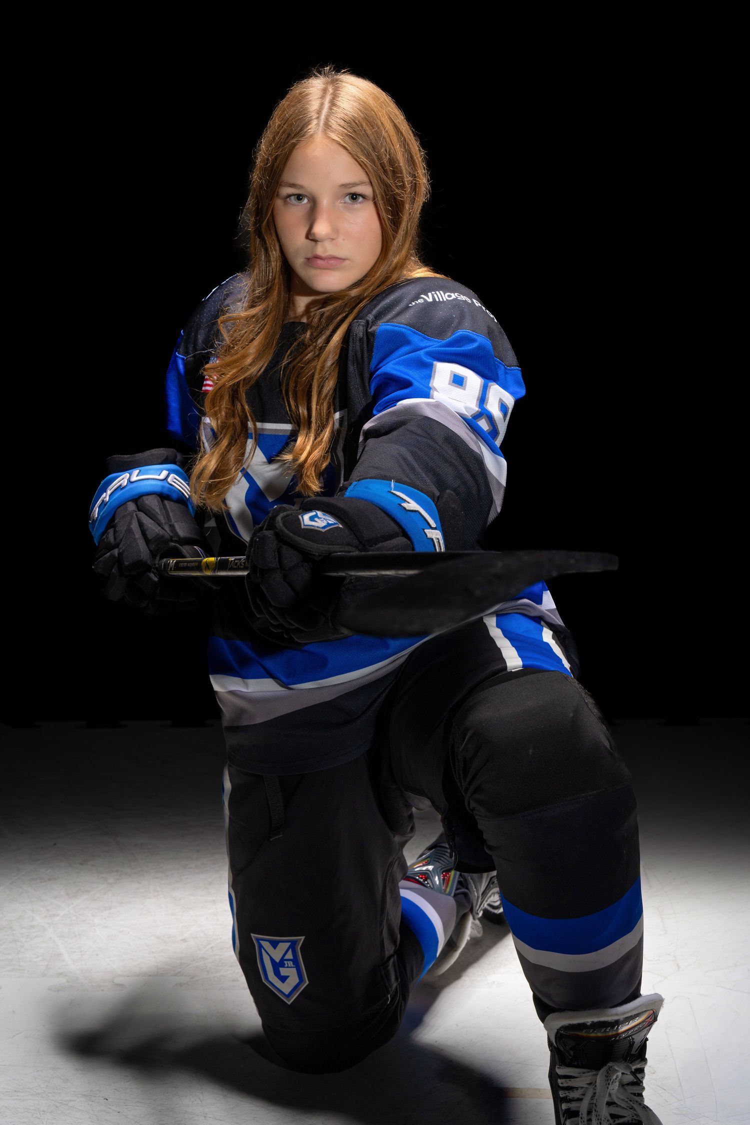 Hockey player in black and blue uniform sits on ice during dramatic studio photoshoot with dark background.
