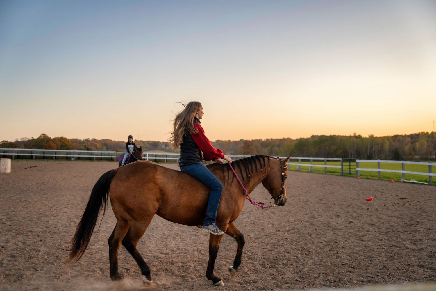 Horses and riders practicing in an outdoor arena during golden hour.