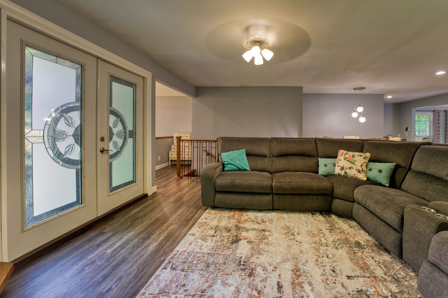 Spacious living room with dark hardwood floors, gray sectional sofa, colorful pillows, area rug, and French doors with decorative glass.