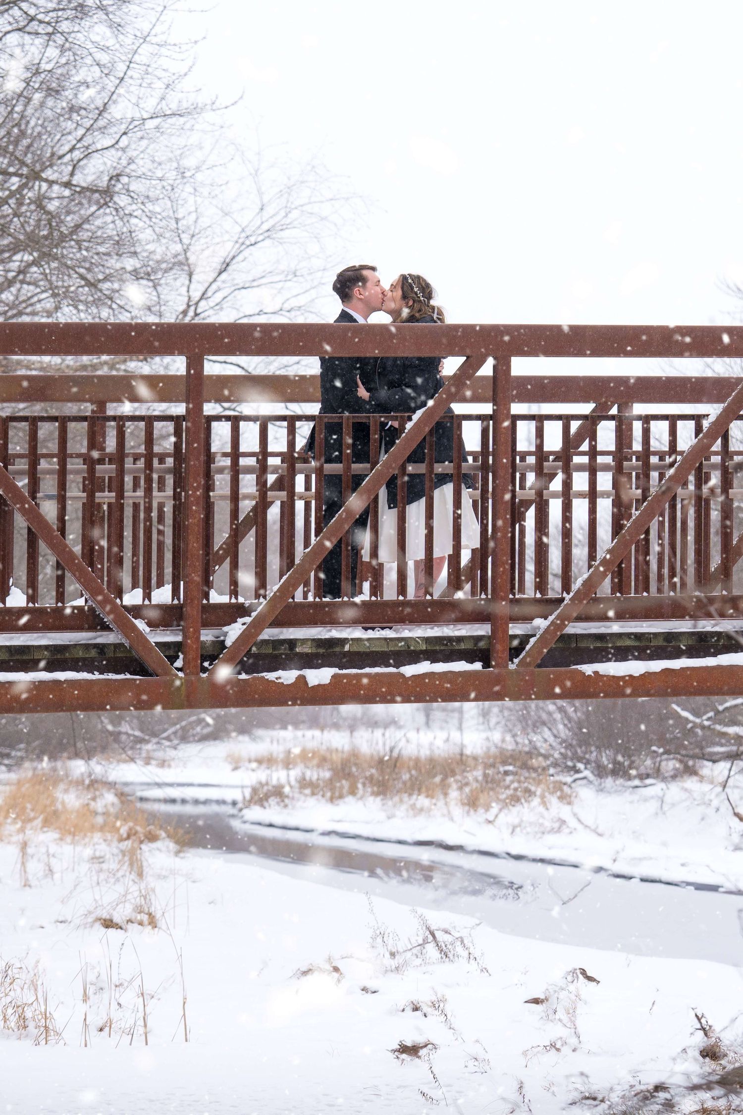A couple shares a romantic moment on a wooden bridge overlooking a snowy winter landscape.