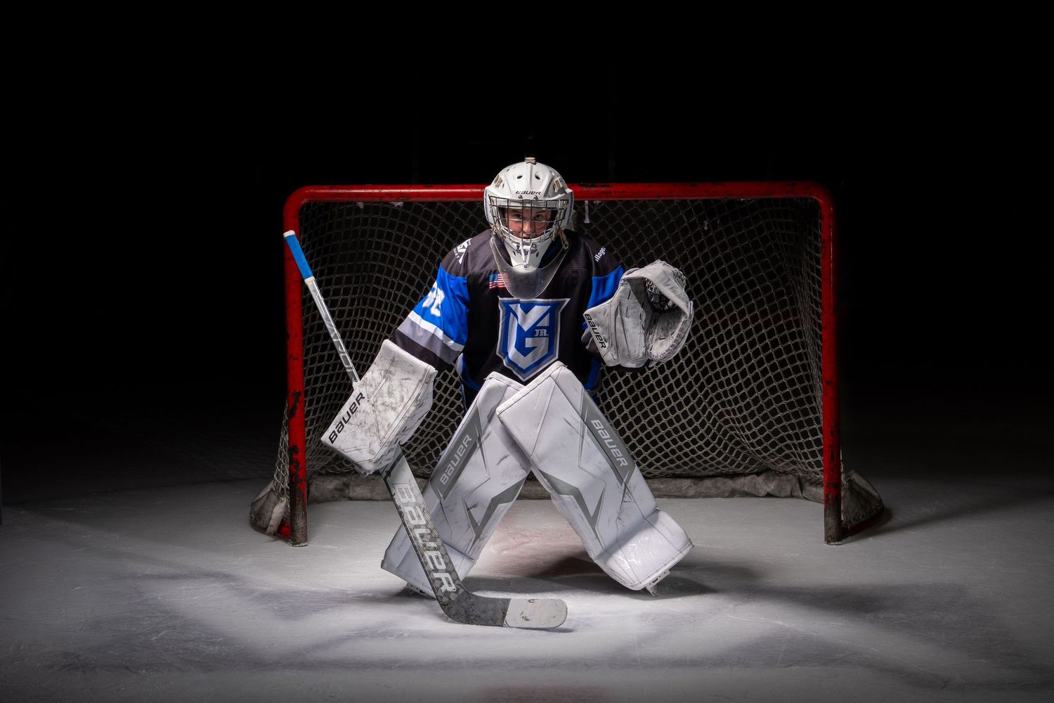 Hockey goalie in white uniform crouching in defensive position in front of net.