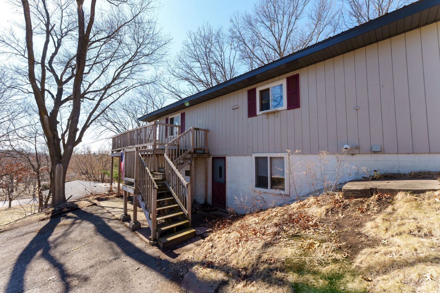 Long white ranch-style house with black trim situated on a sloping terrain among leafless trees.