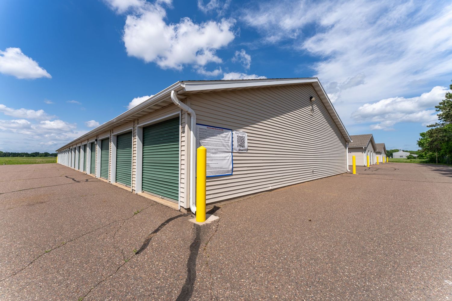 A brown asphalt shingle roof with ridge vents extends across multiple sections under a bright blue sky with white clouds.