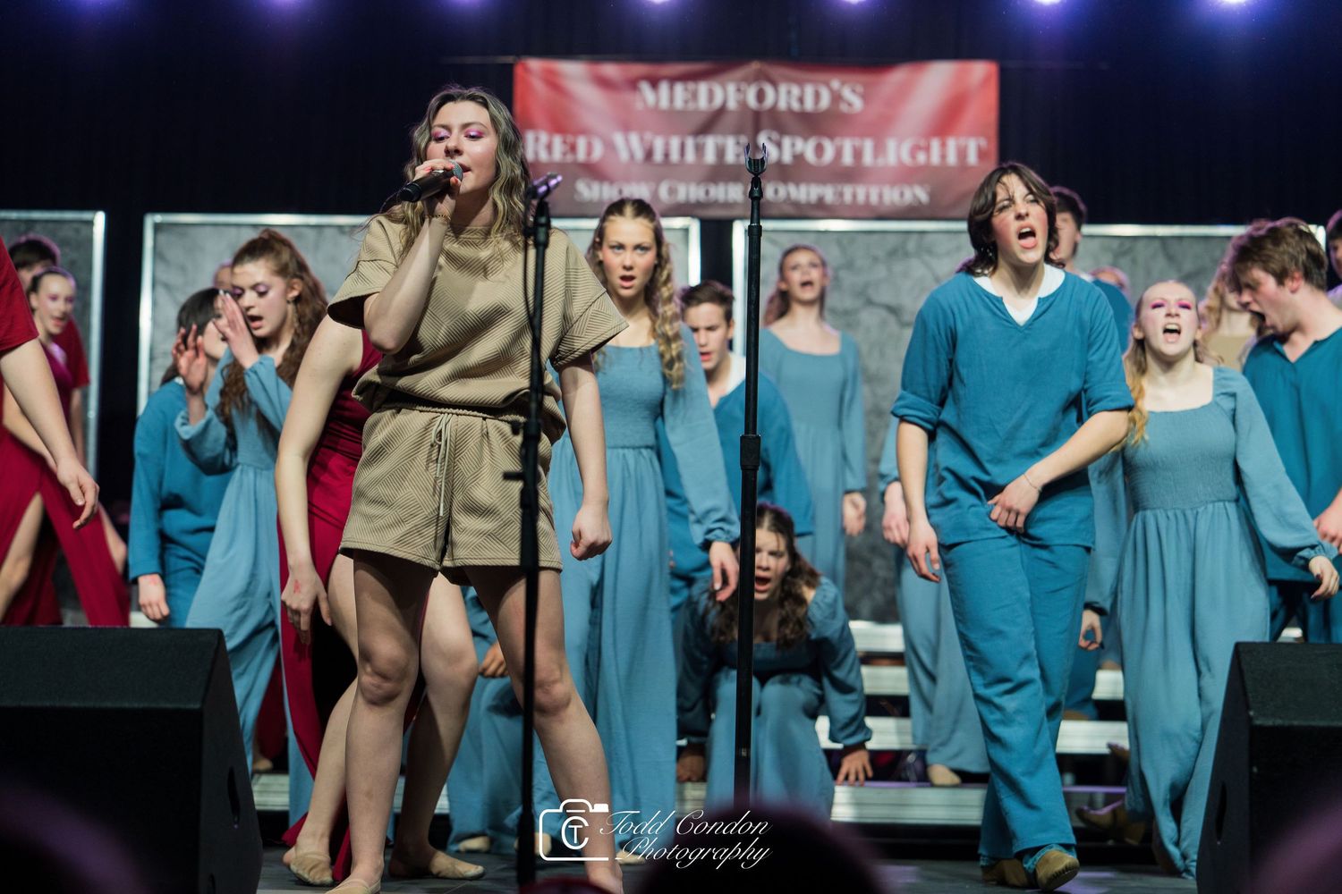 Performers in blue medical scrubs dance and sing on stage during a theatrical production.