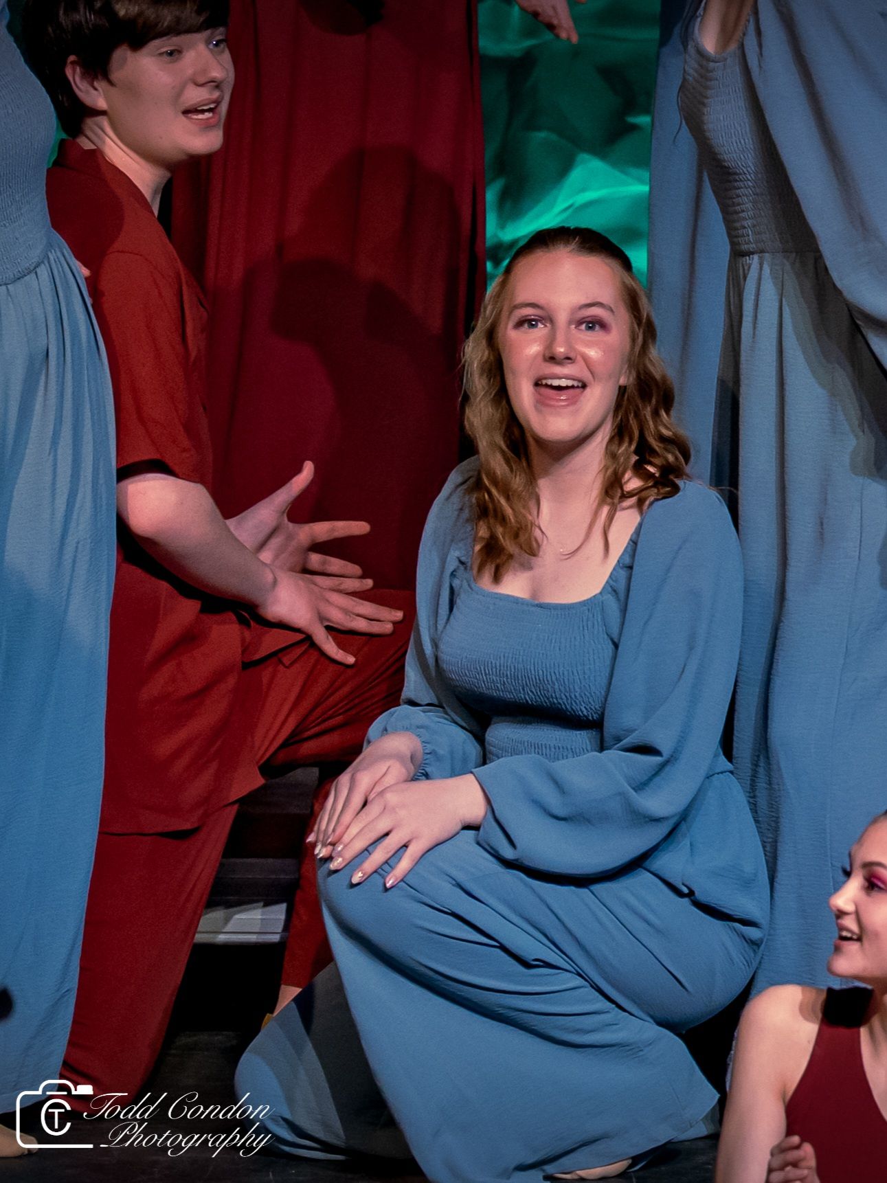 Performers in red and blue costumes interact energetically during a theatrical stage production.