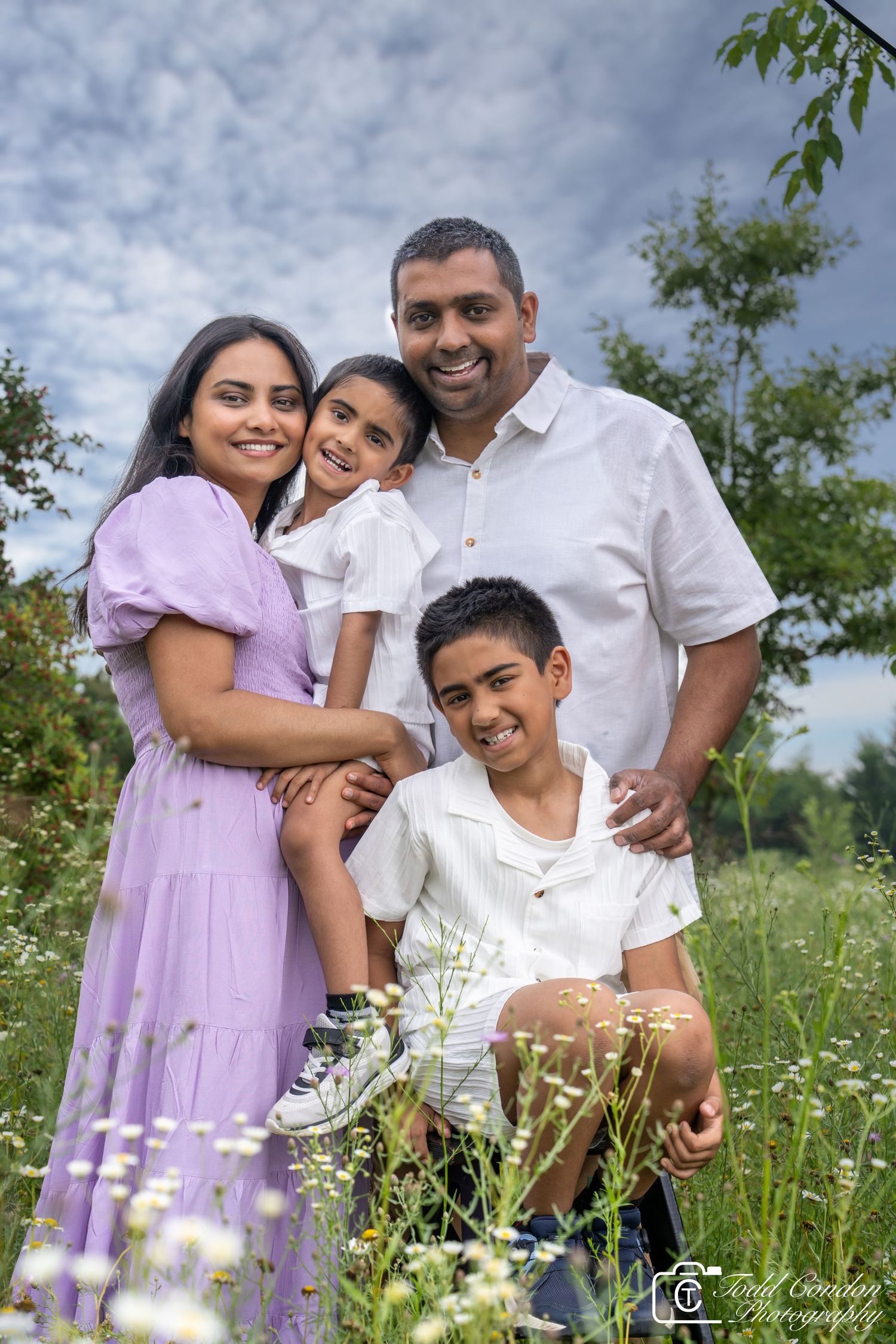 Family wearing white and purple poses together in a summer wildflower field.
