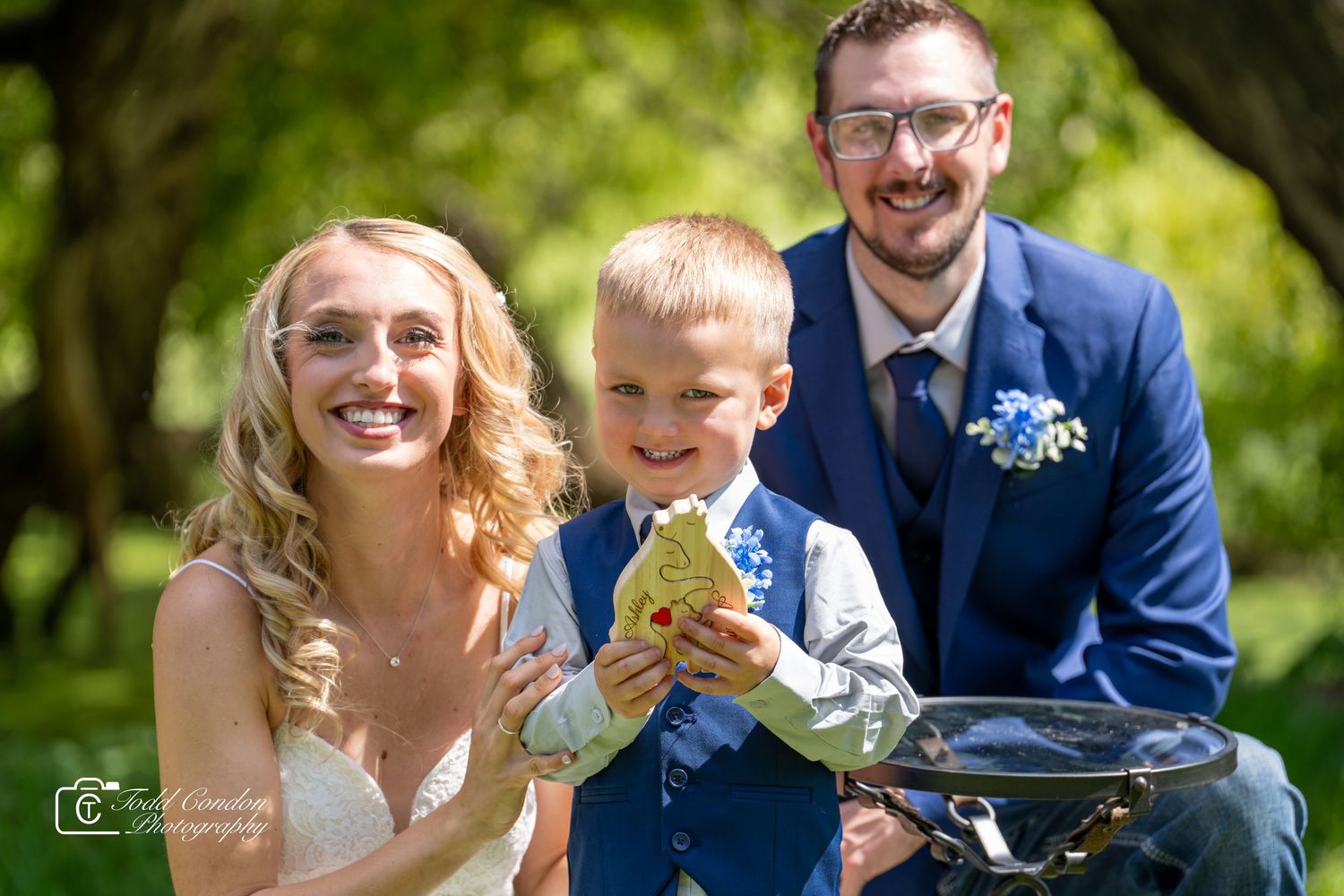 A wedding party poses together outdoors in a natural setting with lush green foliage in the background.