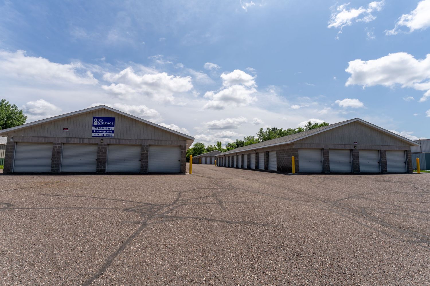 Storage facility with blue garage doors and gravel driveway under partly cloudy sky.