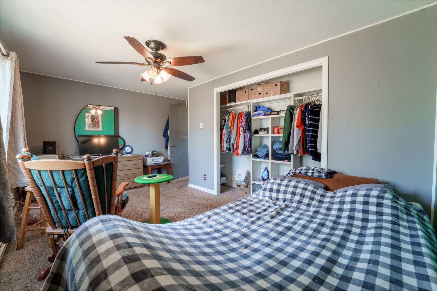 Cozy bedroom interior with buffalo plaid bedding, ceiling fan, and natural light streaming through windows.