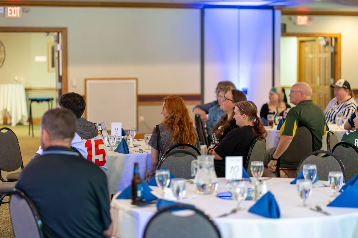 Business professionals seated at round tables in a conference room with blue accent lighting.