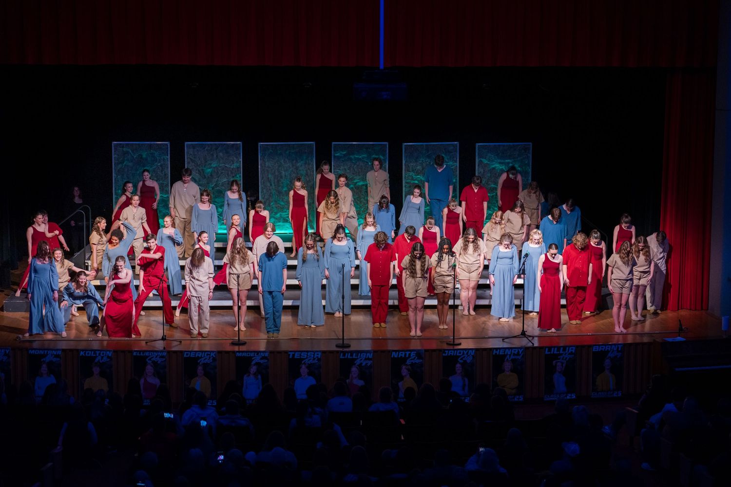 Stage performers in red and white costumes stand in formation during a theatrical production under blue lighting.