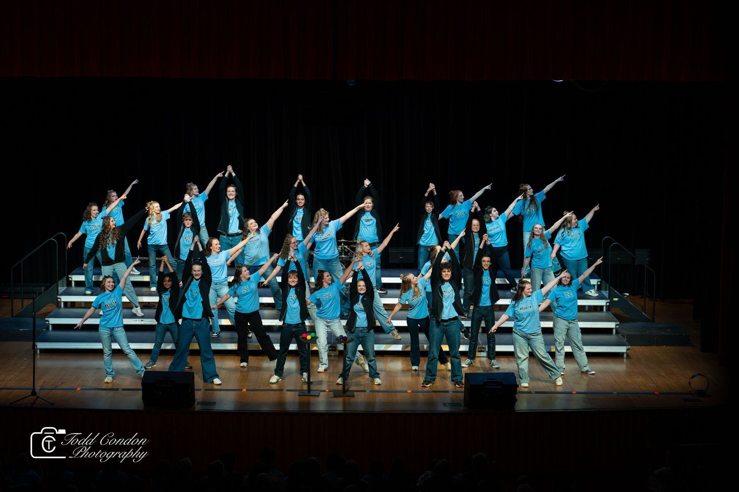 Dance performers in bright blue costumes create dynamic formations on a dark stage during a synchronized performance.