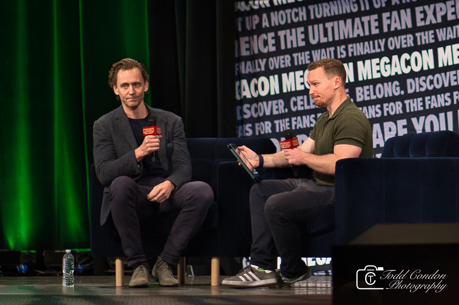 People on stage participate in a panel discussion at a conference with green lighting and text on the wall behind them.