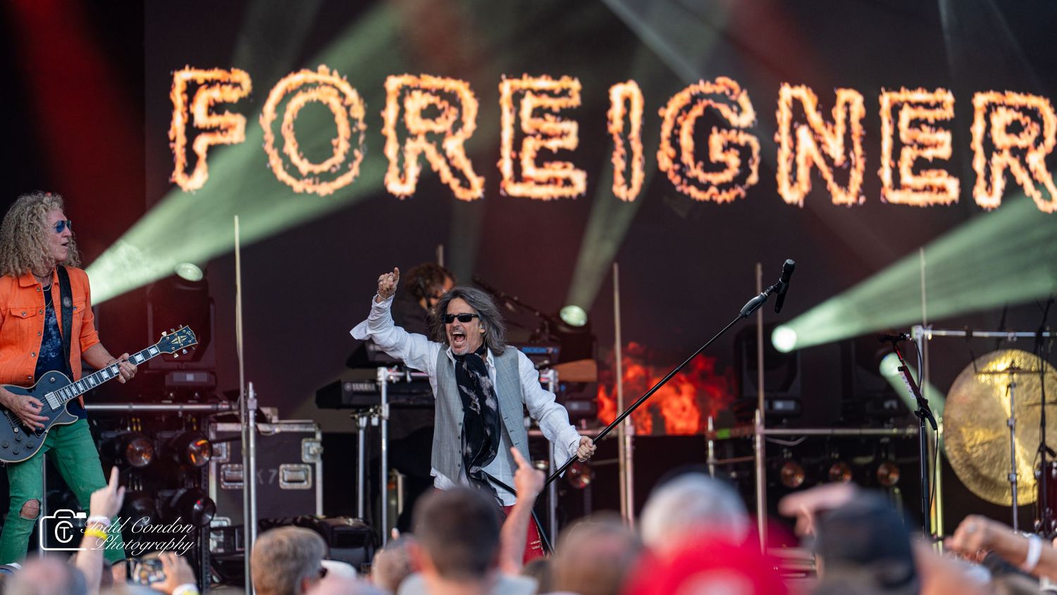 Rock band Foreigner performs live on stage with illuminated sign and green lighting effects during a concert performance.