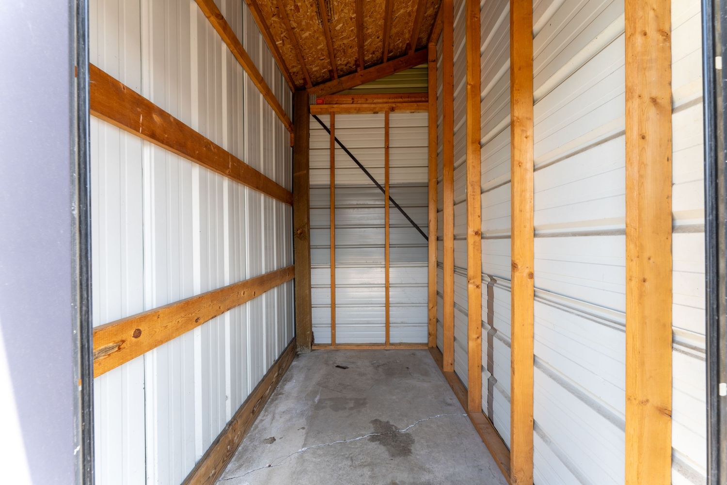 Interior view of an empty storage unit with white walls, wooden support beams, and concrete flooring.