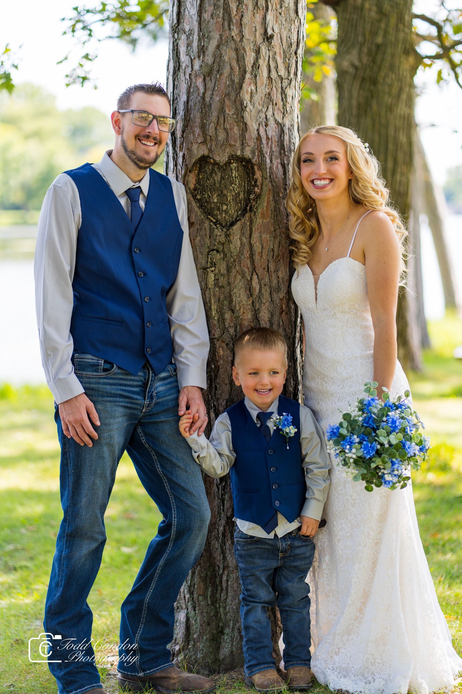 Wedding party in blue and white attire poses casually against trees in an outdoor setting.