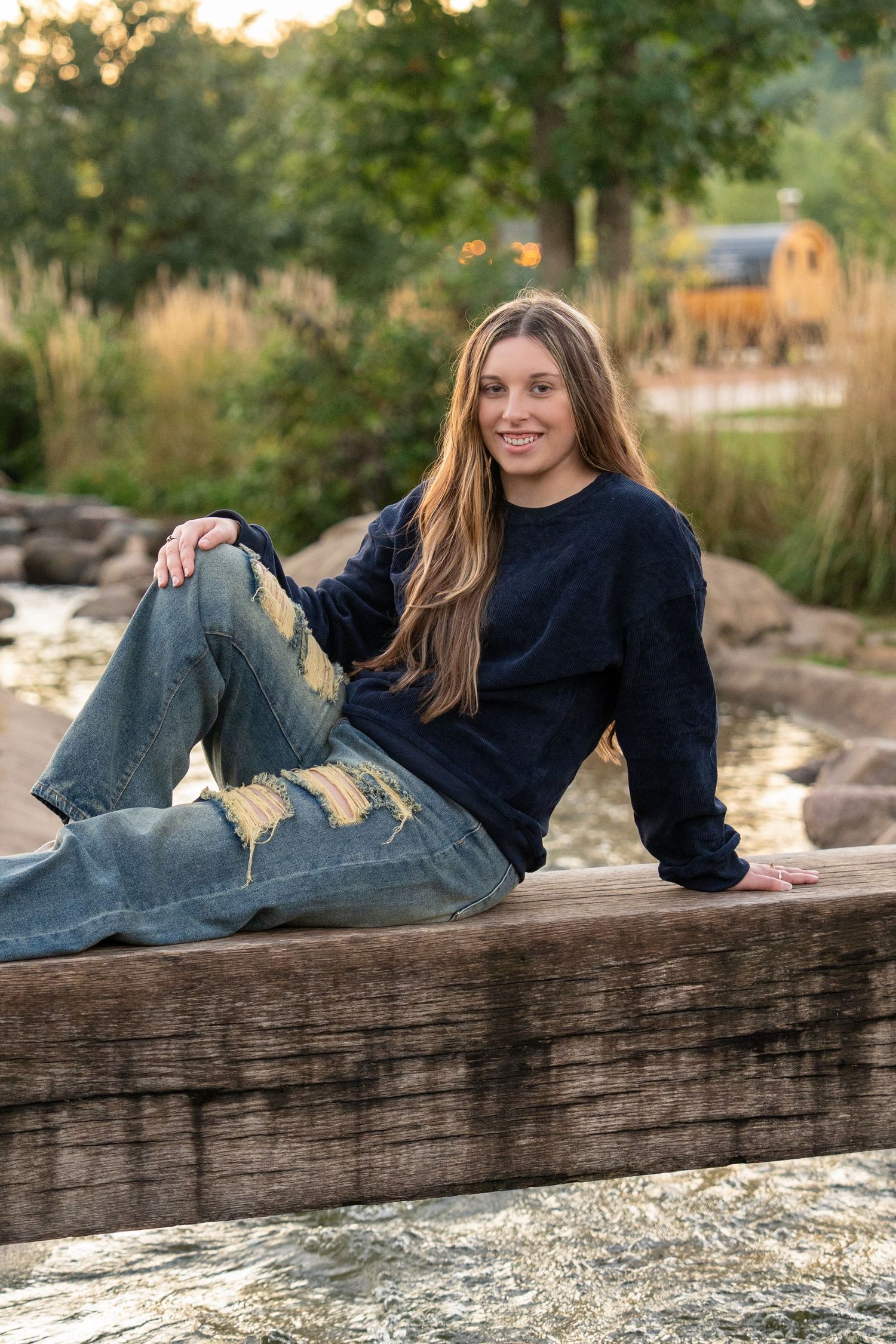 Casual outdoor portrait series showing someone relaxing on a rustic wooden ledge at sunset in a navy sweater and jeans.