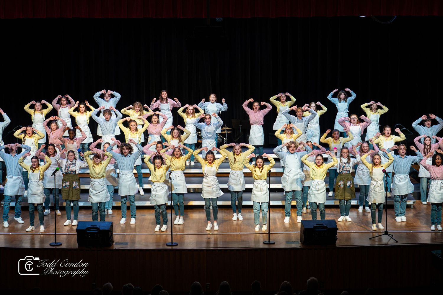 Dancers in white and blue costumes perform synchronized movements on stage during a group performance.