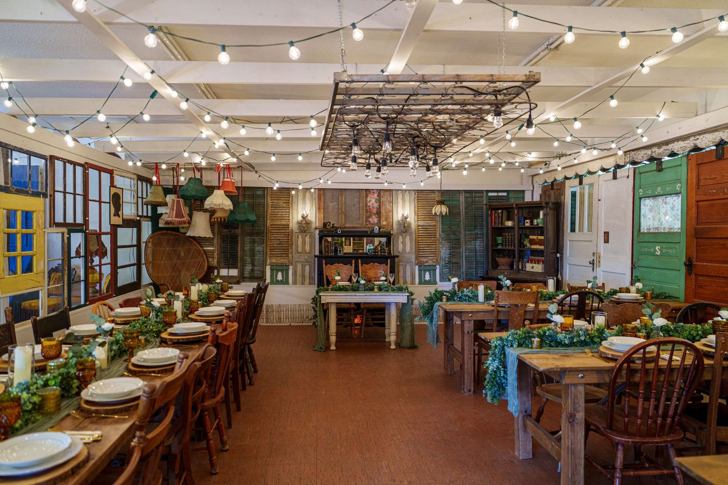 A long restaurant dining room with string lights overhead and wooden tables arranged in rows under warm lighting.