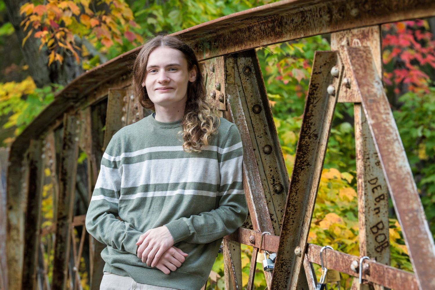 A person in a striped sweater stands on a rustic bridge surrounded by colorful autumn foliage.